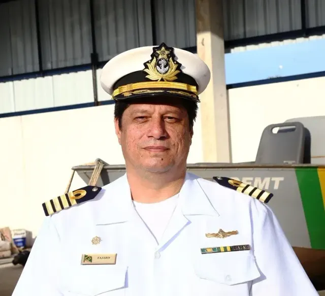 Alessandro Fajard de farda branca e quepe da Marinha, diante de uma lancha